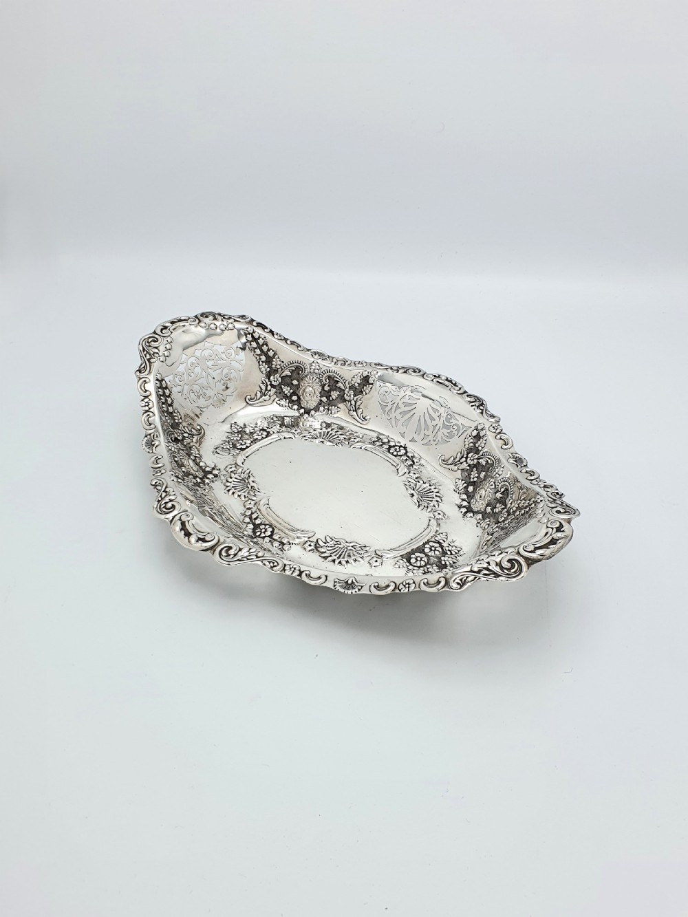 An oval Edwardian solid sterling silver serving dish featuring intricate pierced fretwork sides, scrolled borders, and relief floral decoration.