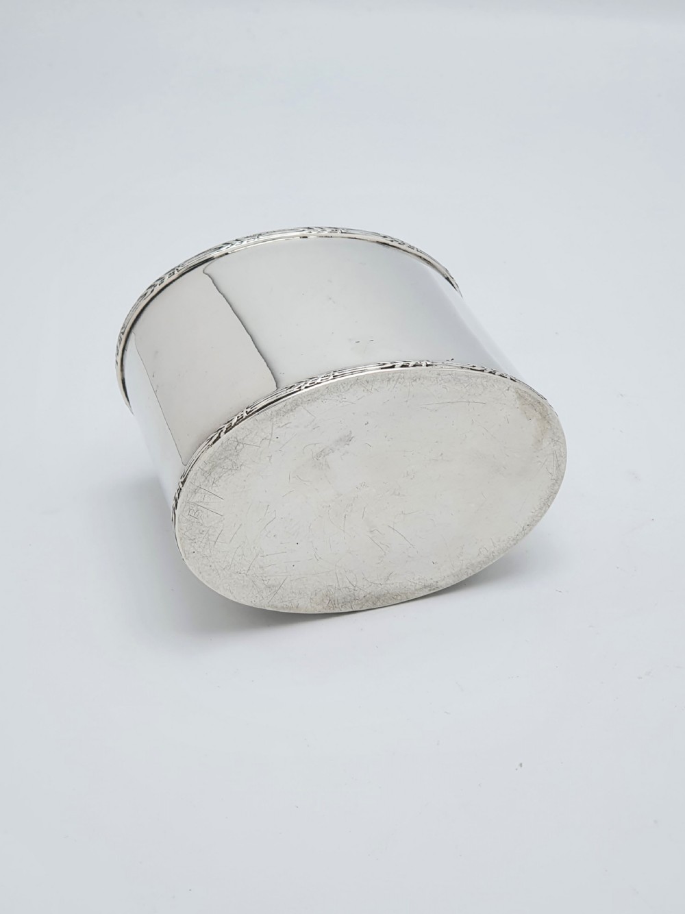 An oval sterling silver tea caddy with a cylindrical push-on cap, engraved leaf borders, and London hallmarks stamped on the front. View III