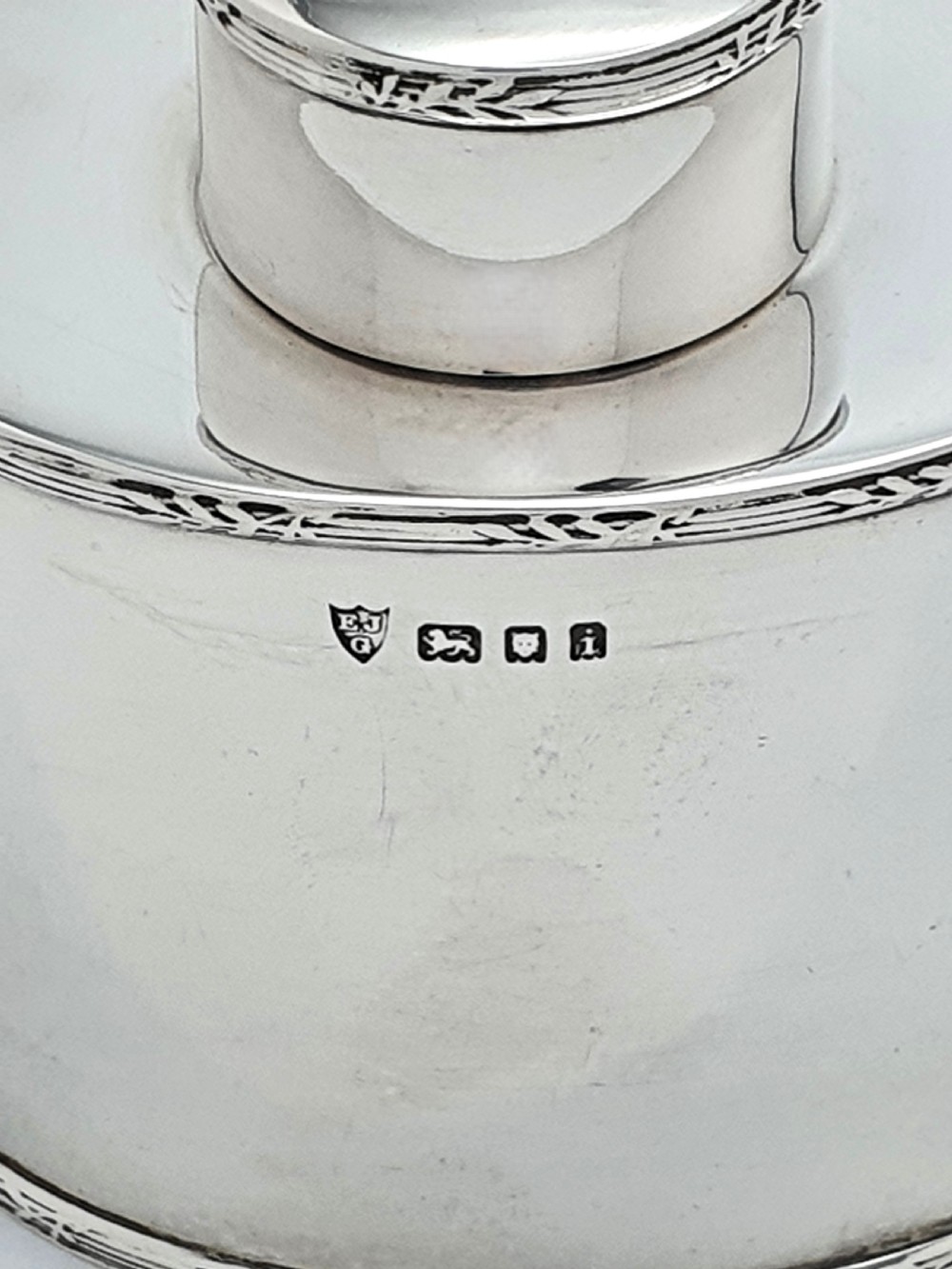 An oval sterling silver tea caddy with a cylindrical push-on cap, engraved leaf borders, and London hallmarks stamped on the front. View IV