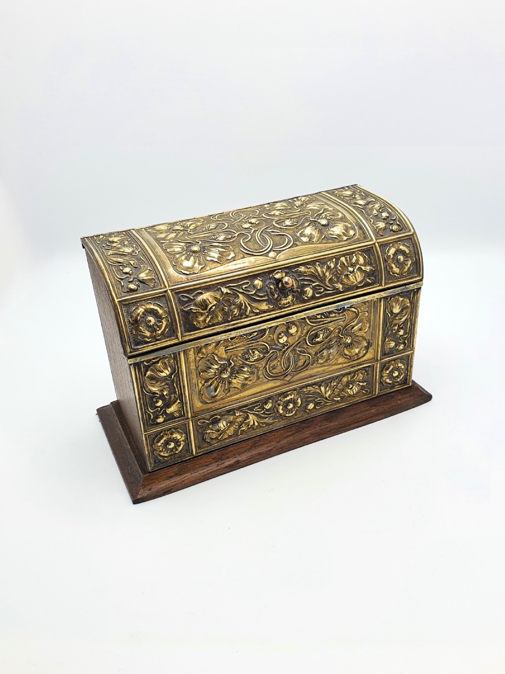 An Edwardian Art Nouveau document box featuring embossed floral brass panels over a dark timber base with a domed lid.