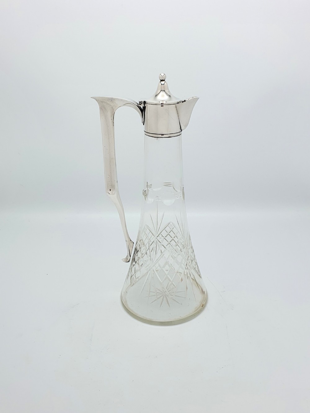 An Edwardian silver-plated claret jug featuring a conical cut crystal glass body, hinged silver lid, and tall angular handle.