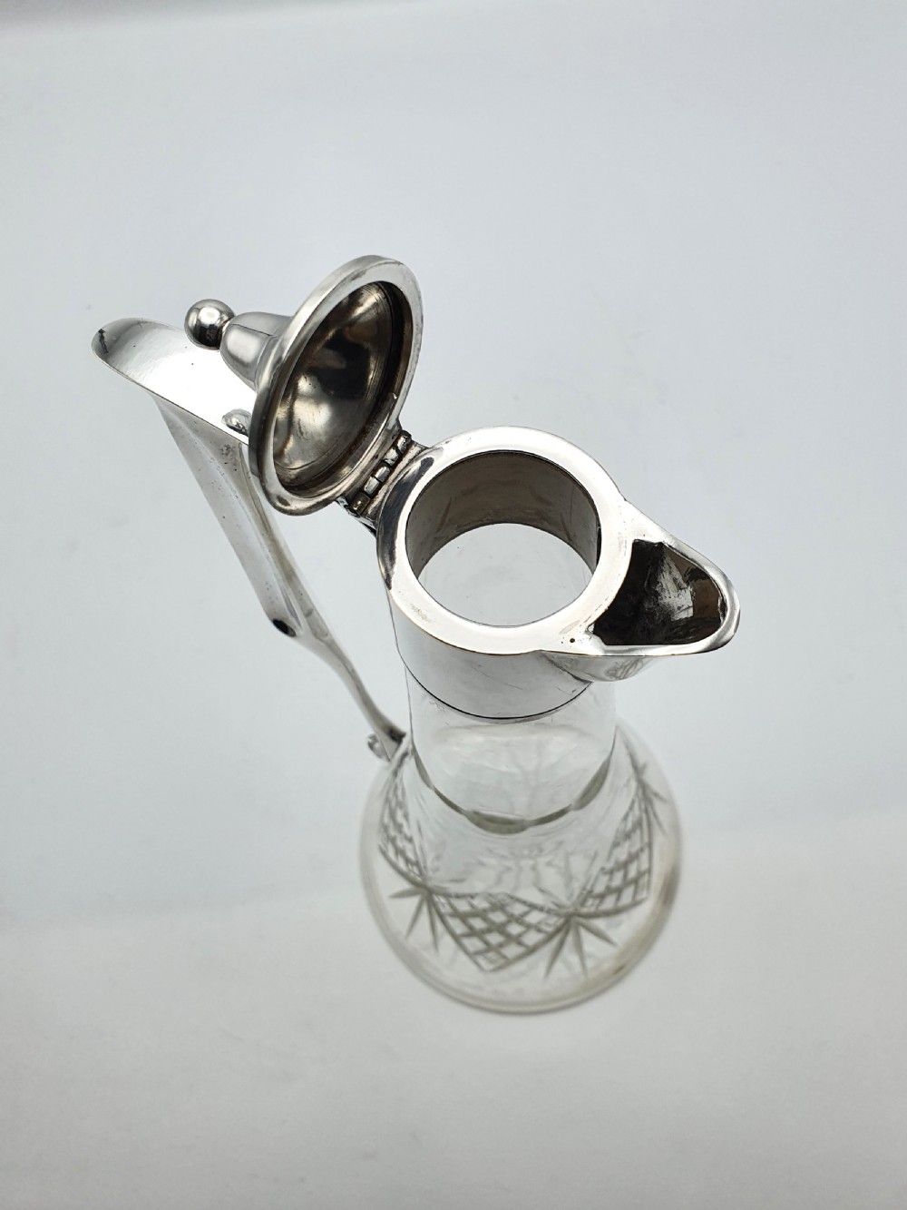 An Edwardian silver-plated claret jug featuring a conical cut crystal glass body, hinged silver lid, and tall angular handle. View II