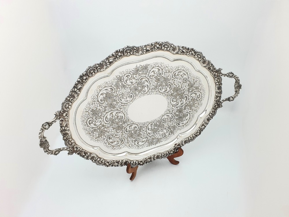 An ornate oval late Victorian silver serving tray featuring twin handles, an intricate hand-engraved scrollwork centre, and a cast shell border.