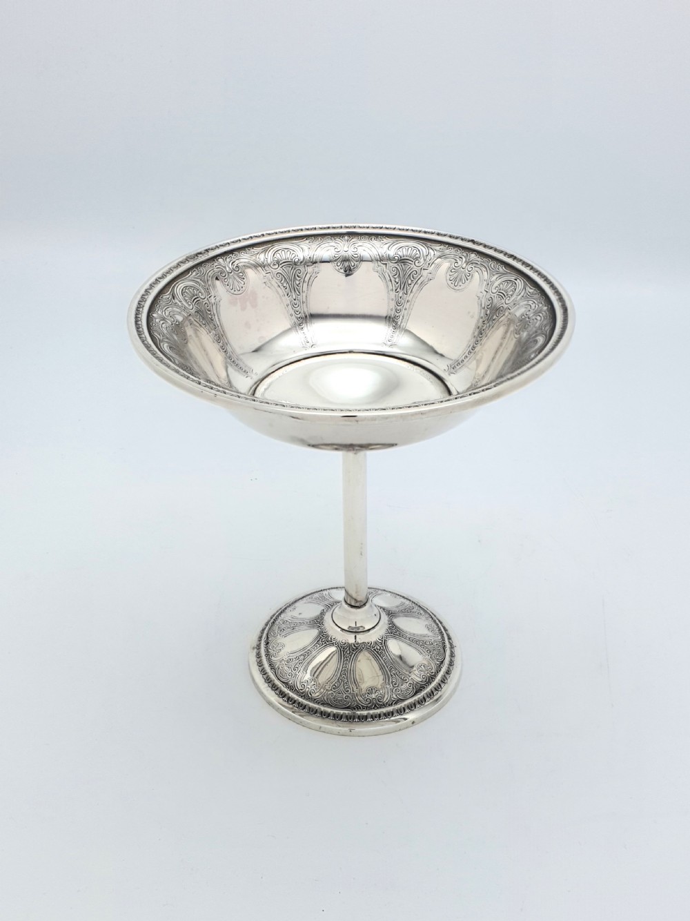 A tall sterling silver comport featuring an ornate engraved interior rim, a slender central stem, and a patterned domed circular foot.