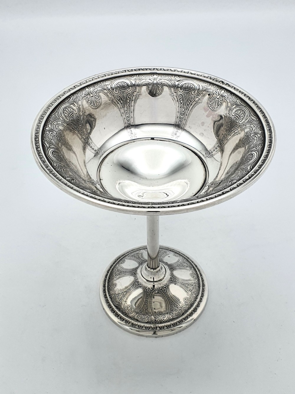 A tall sterling silver comport featuring an ornate engraved interior rim, a slender central stem, and a patterned domed circular foot. View II