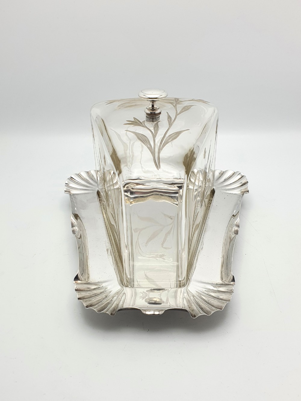 A wedge-shaped glass cheese dome with etched botanical details resting on a contoured silver-plated tray. View II
