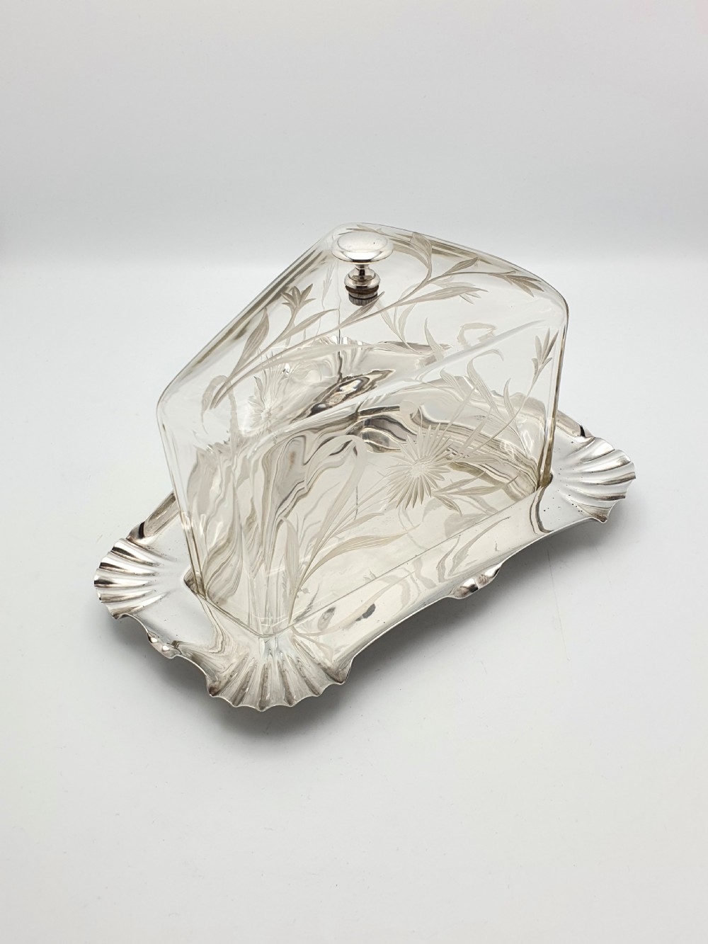 A wedge-shaped glass cheese dome with etched botanical details resting on a contoured silver-plated tray. View III