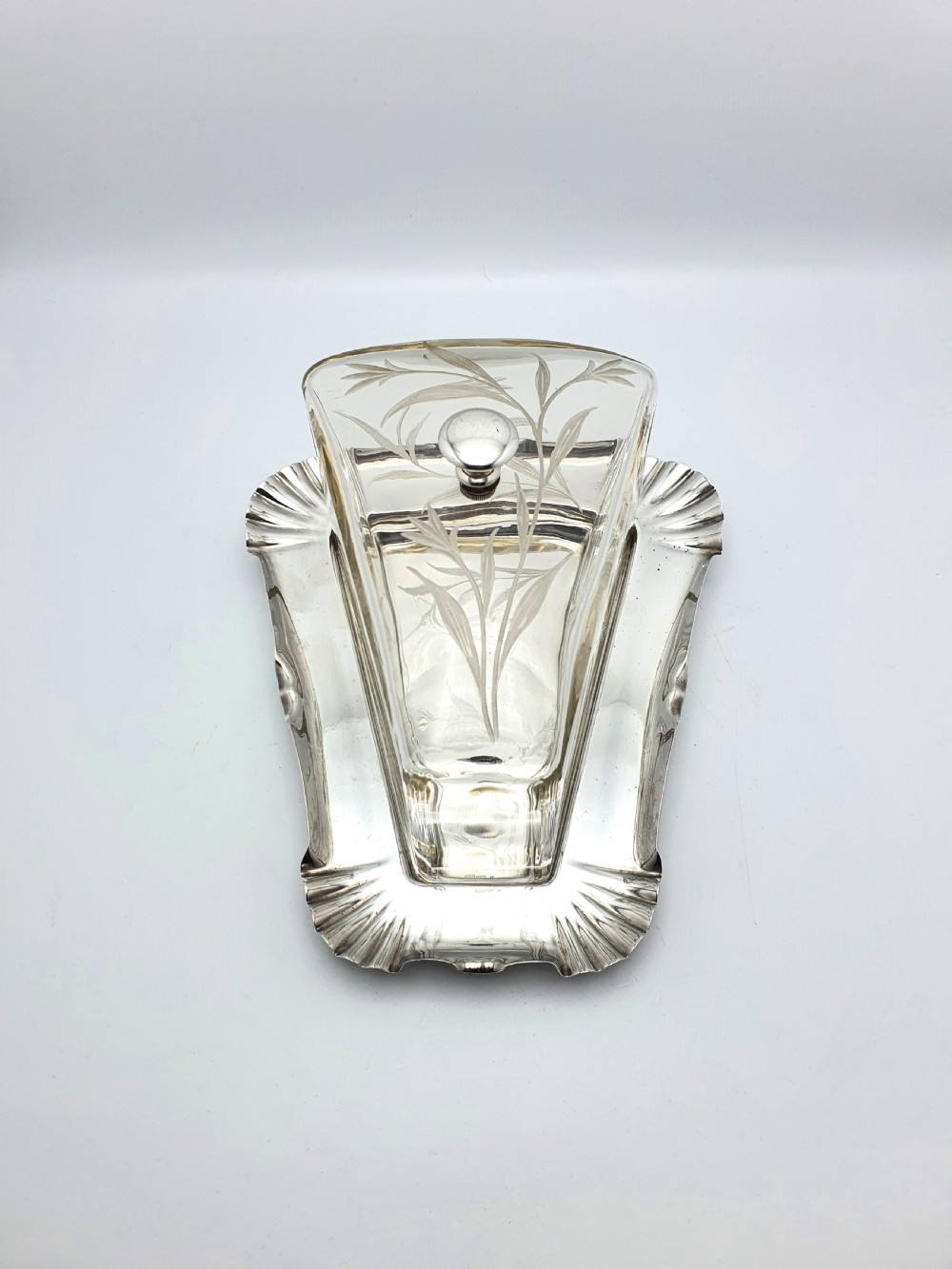 A wedge-shaped glass cheese dome with etched botanical details resting on a contoured silver-plated tray. View IV