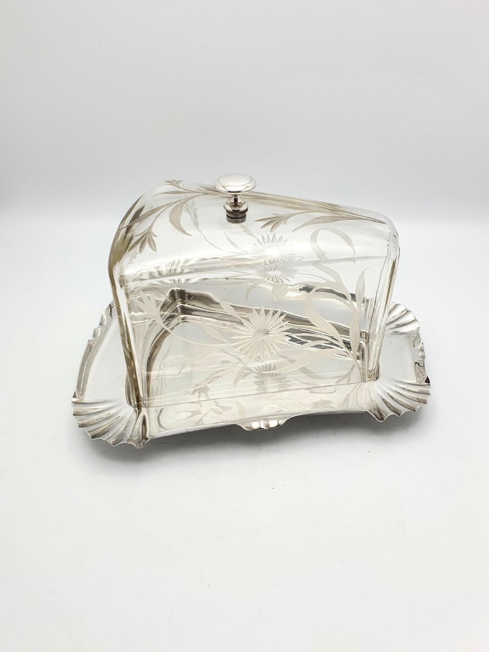 A wedge-shaped glass cheese dome with etched botanical details resting on a contoured silver-plated tray. View V