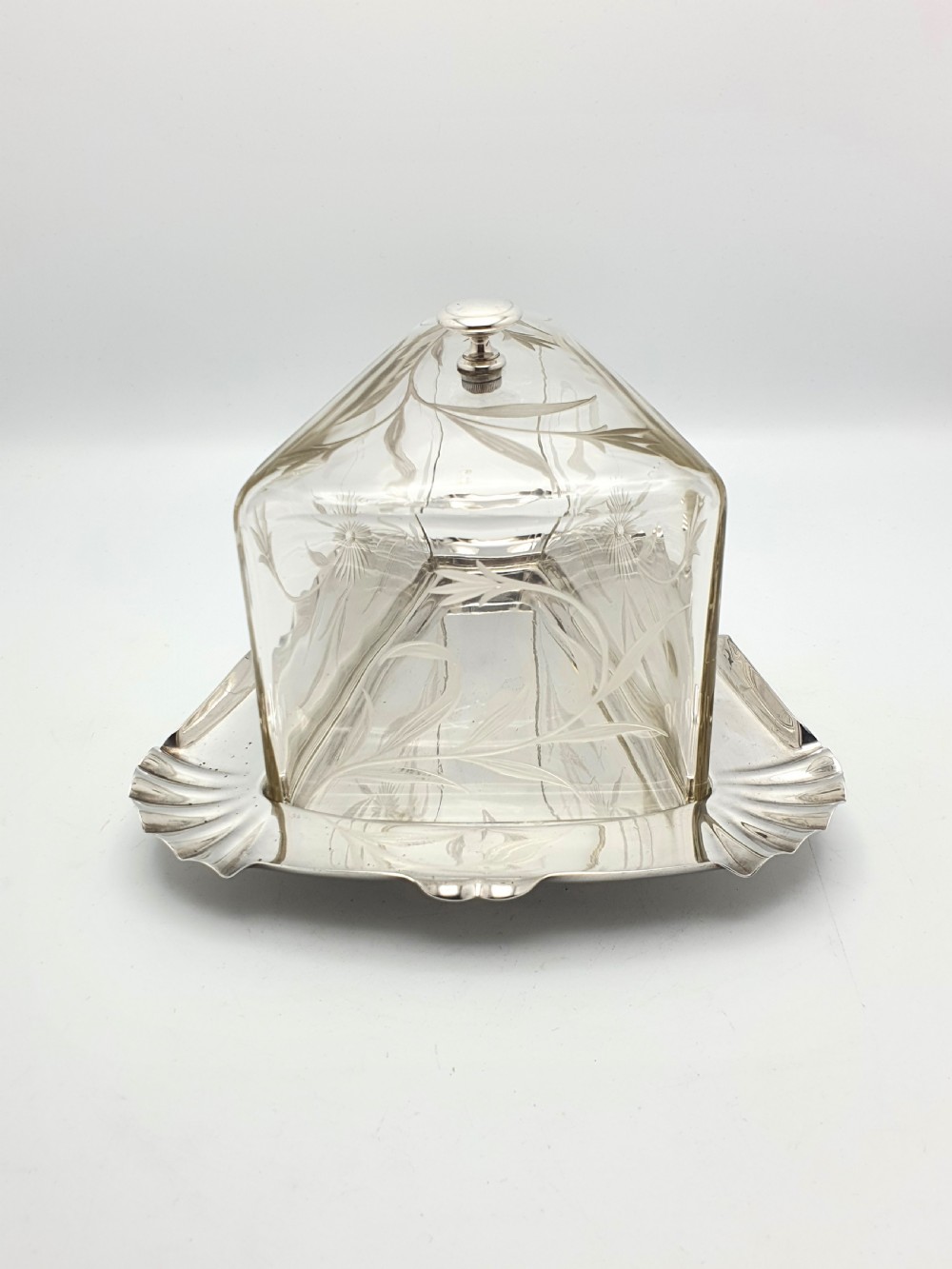 A wedge-shaped glass cheese dome with etched botanical details resting on a contoured silver-plated tray. View VI