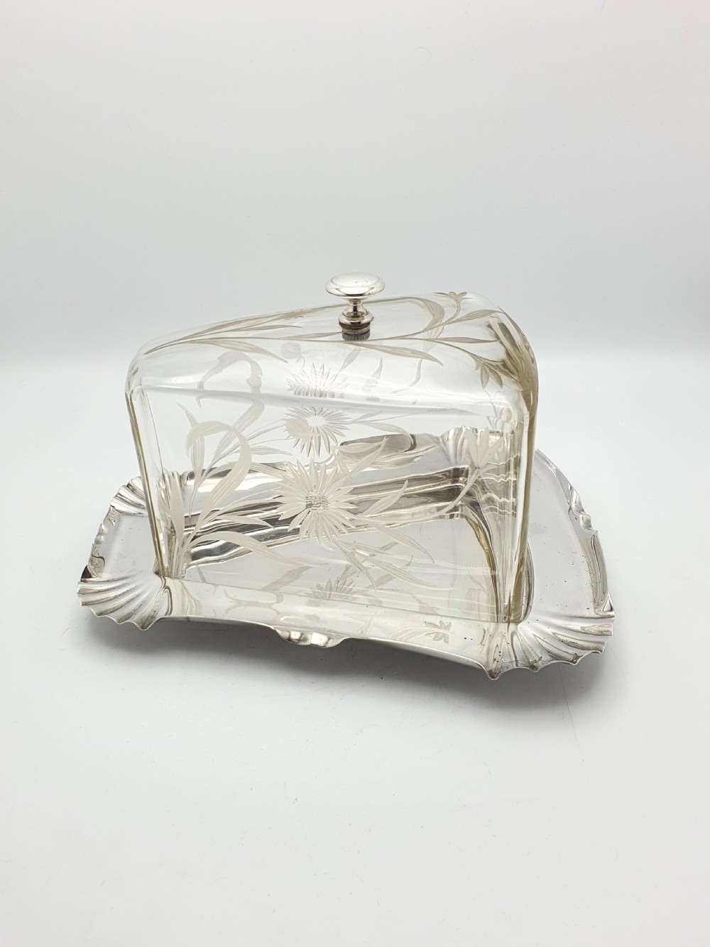 A wedge-shaped glass cheese dome with etched botanical details resting on a contoured silver-plated tray. View VII