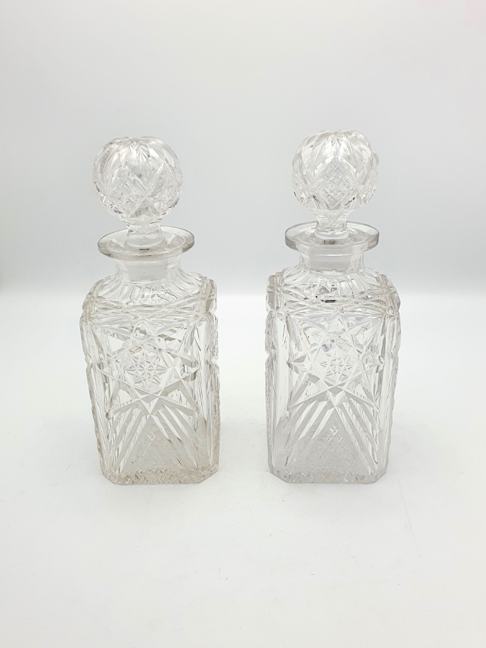 A pair of Edwardian clear cut glass spirit decanters with square bodies, geometric cut patterns, and matching spherical faceted stoppers. View II