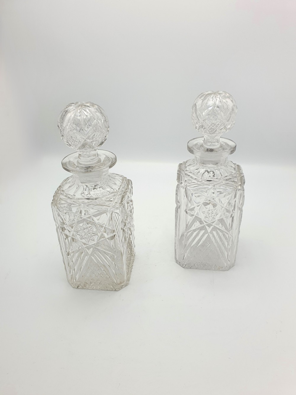 A pair of Edwardian clear cut glass spirit decanters with square bodies, geometric cut patterns, and matching spherical faceted stoppers. View III