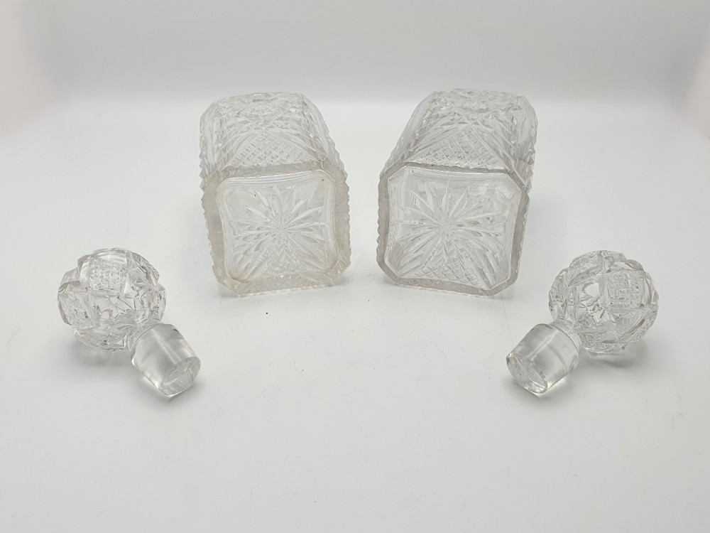 A pair of Edwardian clear cut glass spirit decanters with square bodies, geometric cut patterns, and matching spherical faceted stoppers. View VI