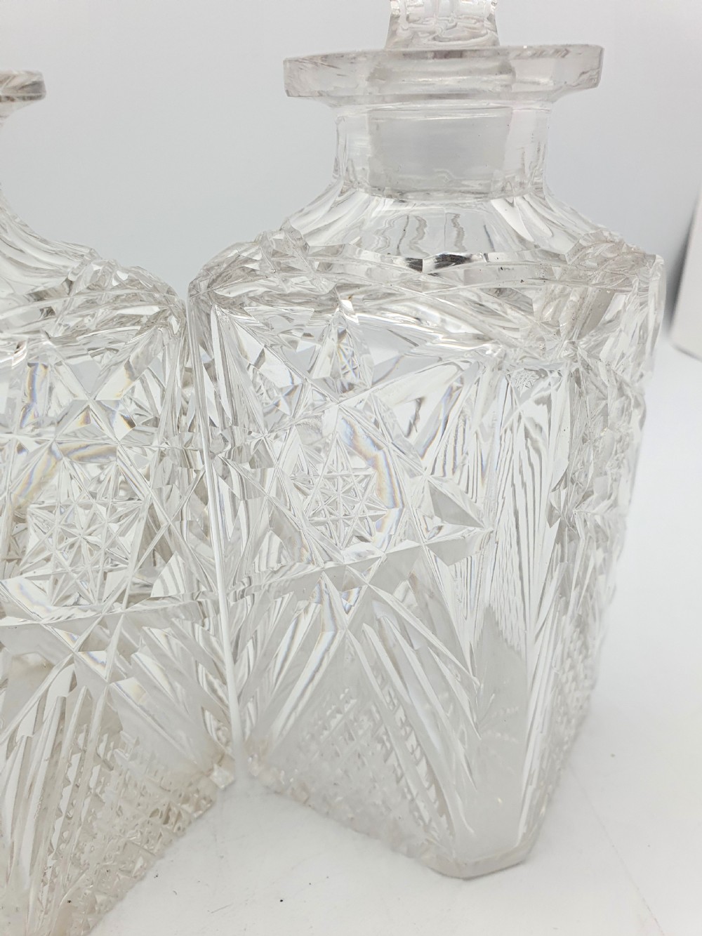 A pair of Edwardian clear cut glass spirit decanters with square bodies, geometric cut patterns, and matching spherical faceted stoppers. View VII