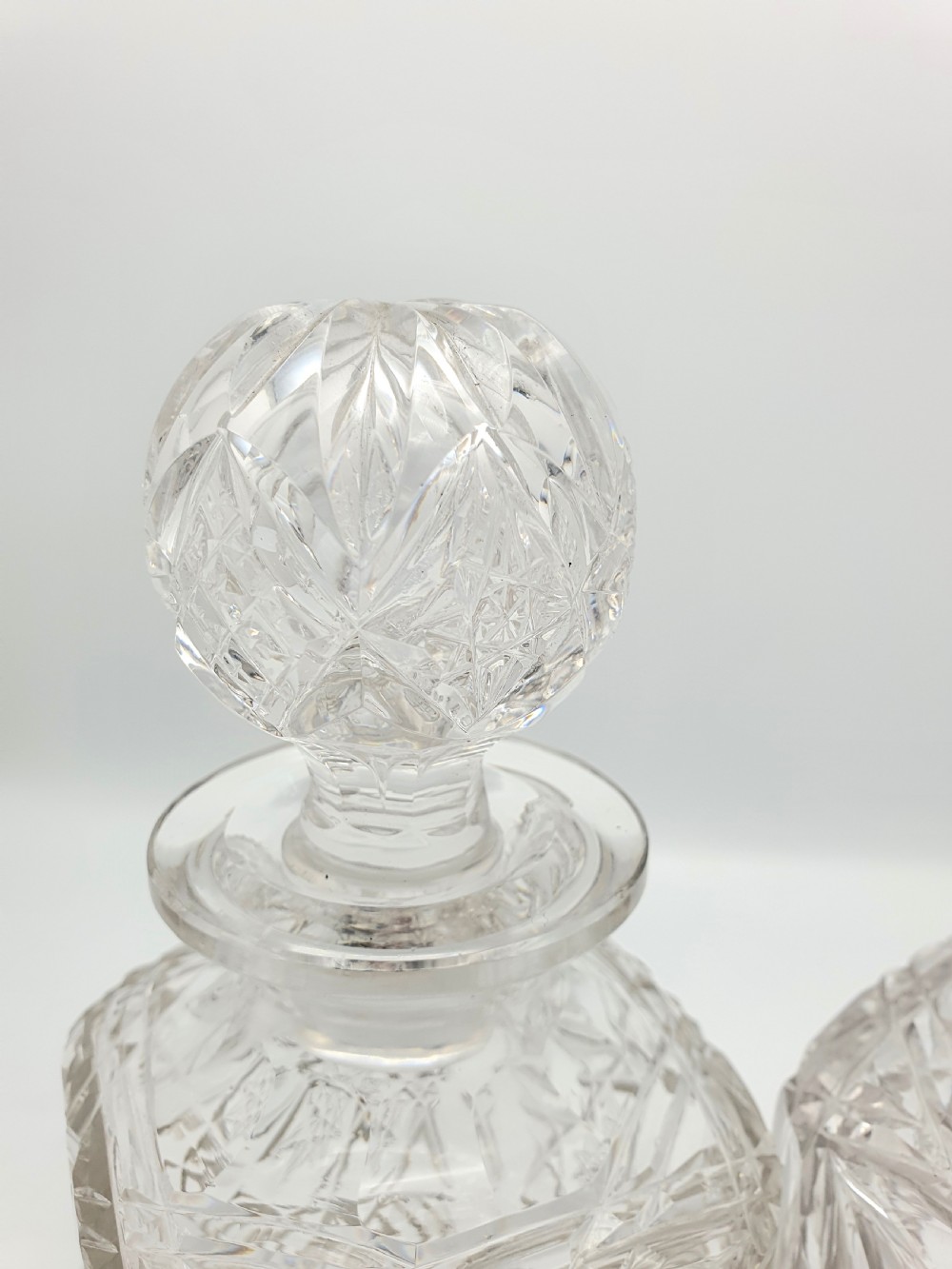 A pair of Edwardian clear cut glass spirit decanters with square bodies, geometric cut patterns, and matching spherical faceted stoppers. View VIII