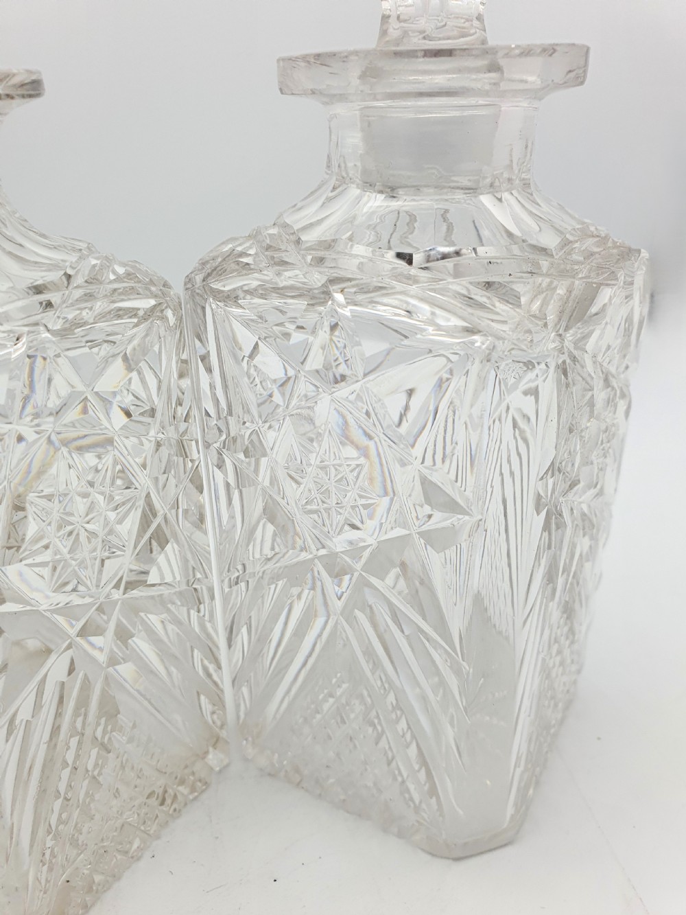 A pair of Edwardian clear cut glass spirit decanters with square bodies, geometric cut patterns, and matching spherical faceted stoppers. View IX