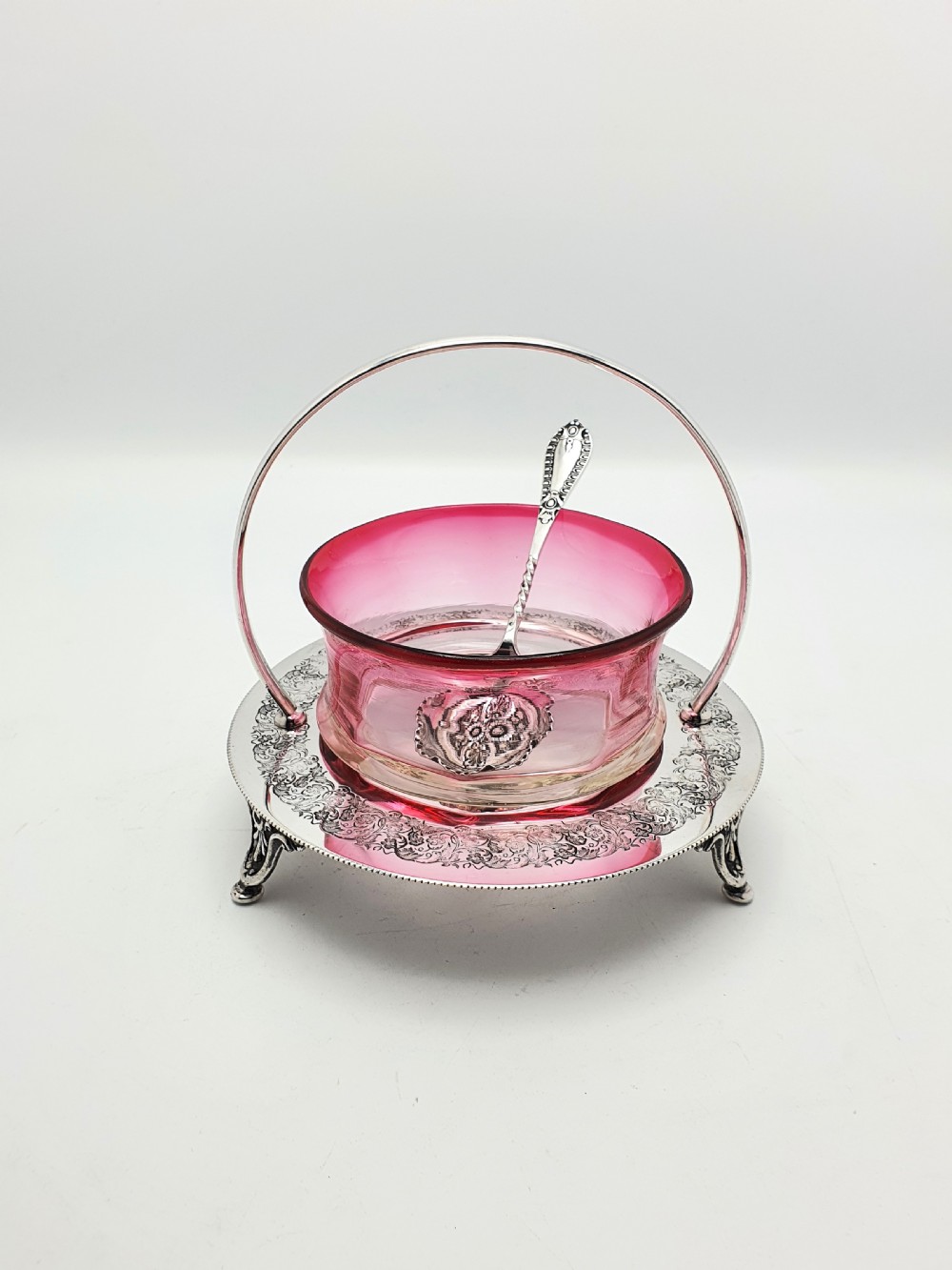 An Edwardian cranberry glass dish resting inside an engraved silver-plated stand with a swing handle and spoon. View III
