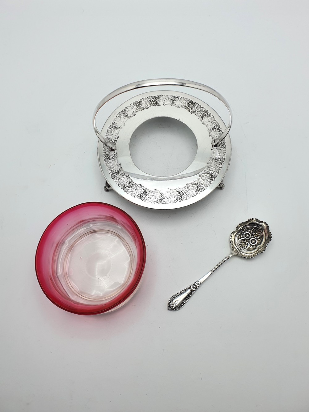An Edwardian cranberry glass dish resting inside an engraved silver-plated stand with a swing handle and spoon. View VI