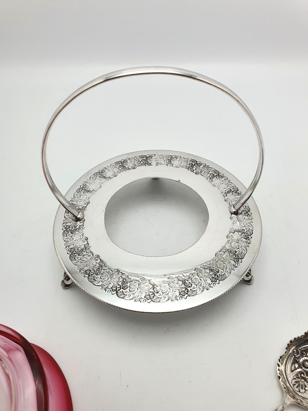 An Edwardian cranberry glass dish resting inside an engraved silver-plated stand with a swing handle and spoon. View IX