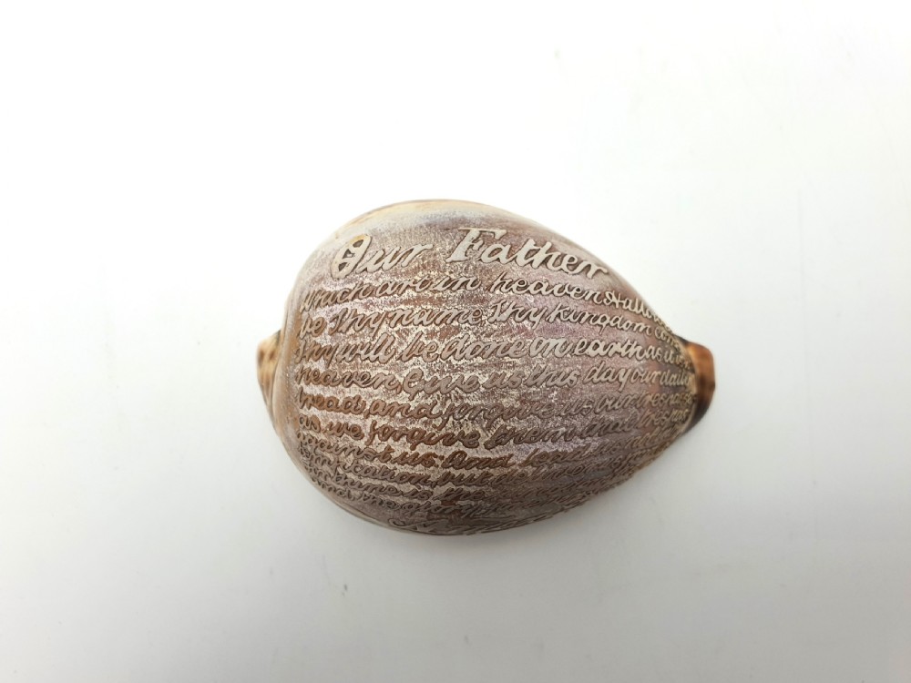 A polished cream and brown cowrie shell intricately etched with calligraphic cursive script detailing the Lords Prayer. View II