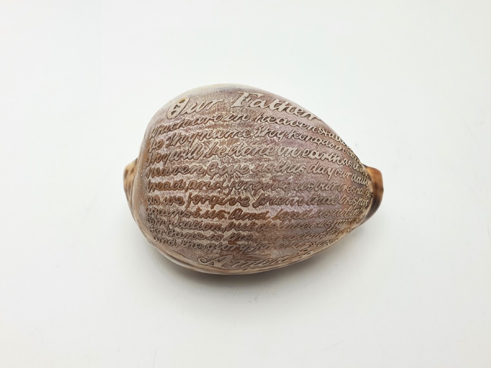 A polished cream and brown cowrie shell intricately etched with calligraphic cursive script detailing the Lords Prayer. View IV