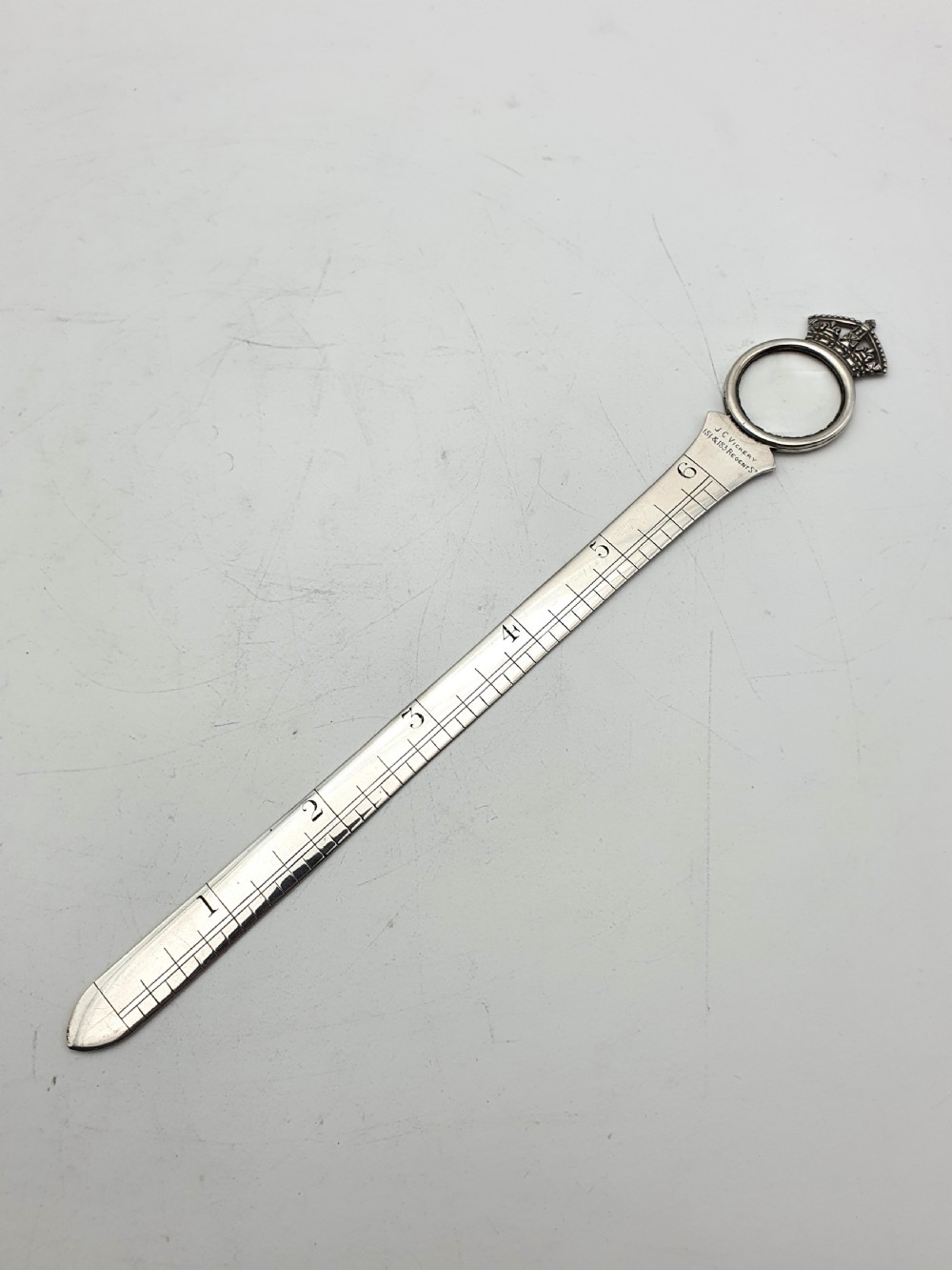 A solid silver Victorian letter opener featuring an engraved ruler edge, makers inscription, and a crown-topped circular finial.