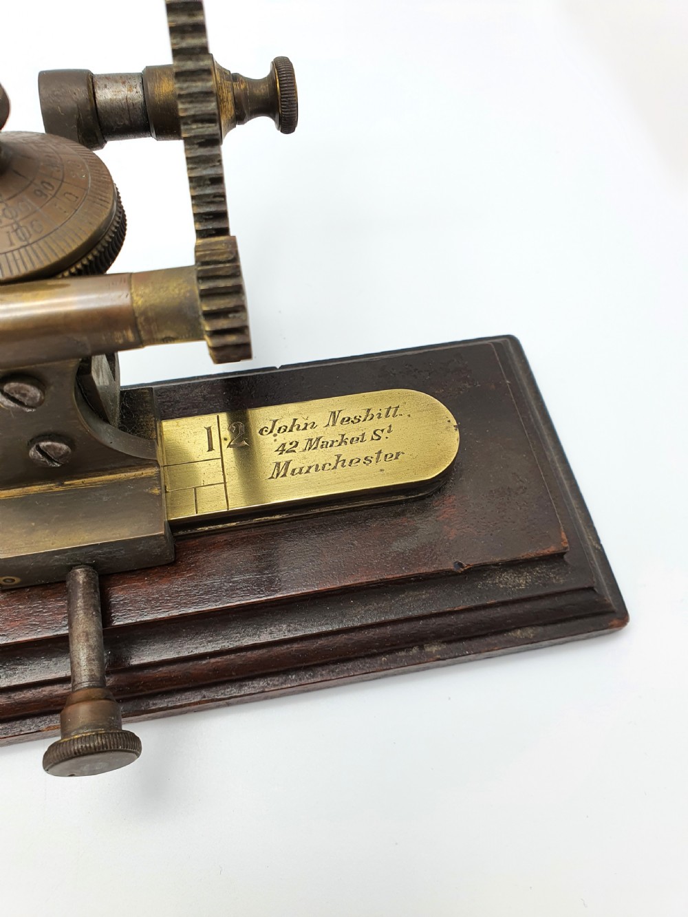 An antique brass thread tester mounted on a dark mahogany base with an engraved ruler scale and geared mechanism. View II