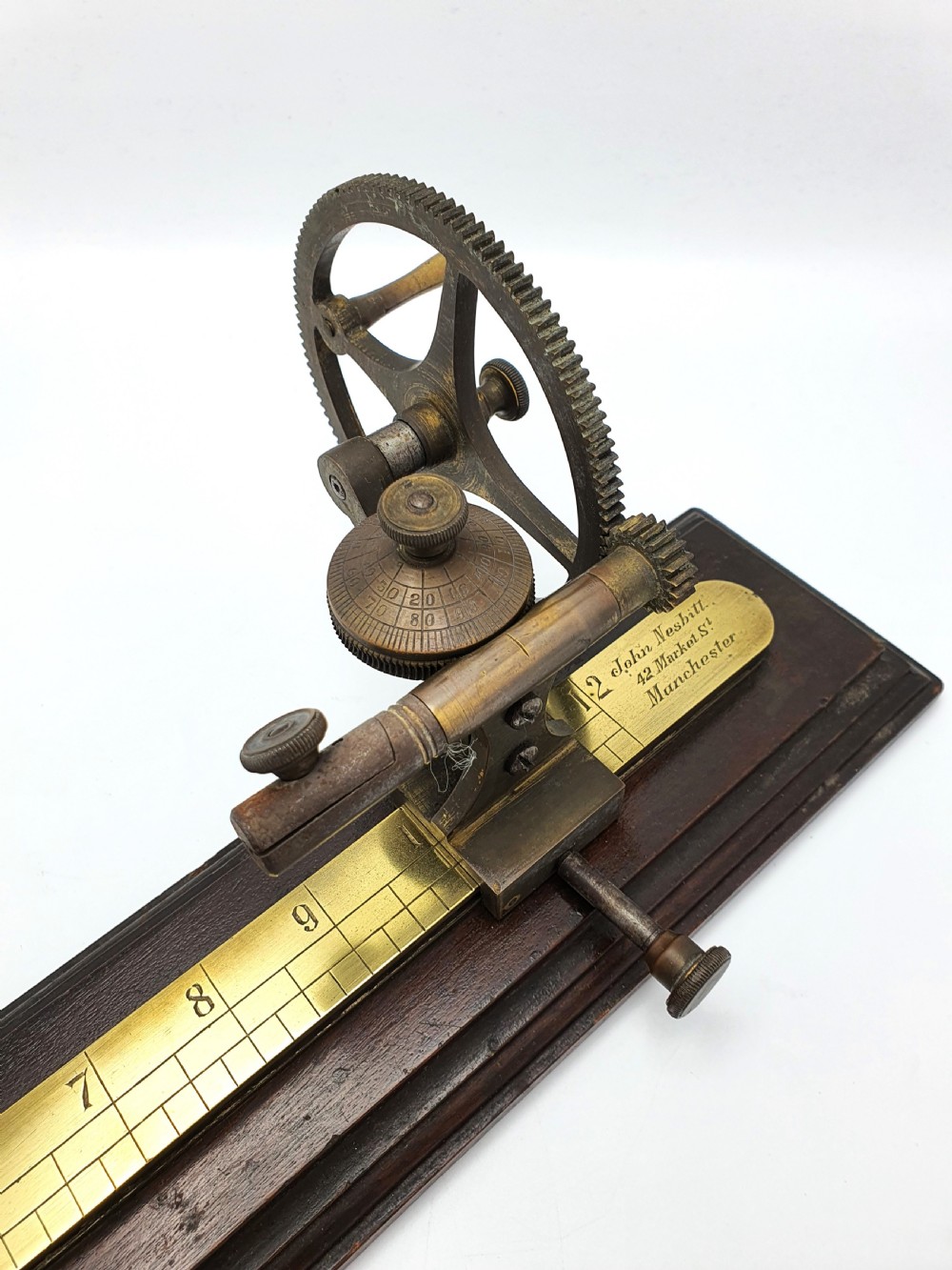 An antique brass thread tester mounted on a dark mahogany base with an engraved ruler scale and geared mechanism. View III