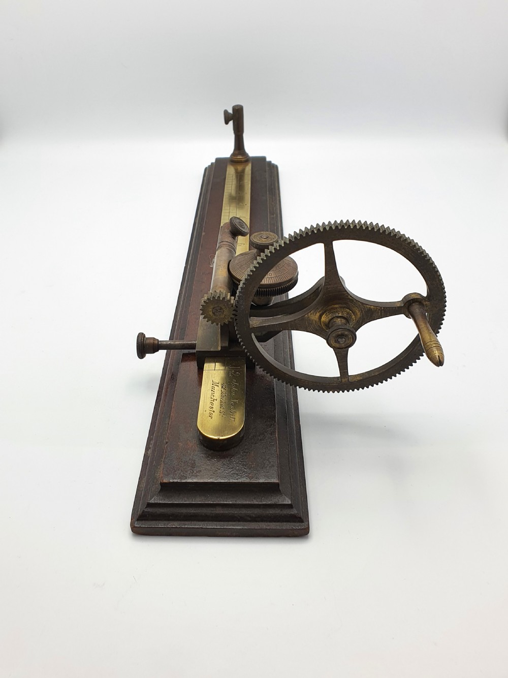 An antique brass thread tester mounted on a dark mahogany base with an engraved ruler scale and geared mechanism. View VI