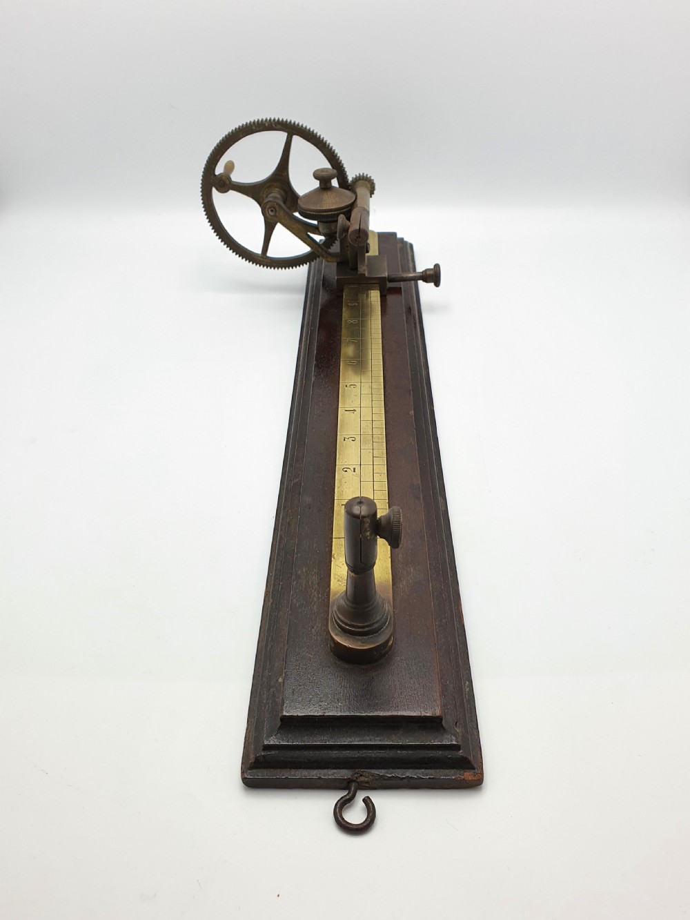 An antique brass thread tester mounted on a dark mahogany base with an engraved ruler scale and geared mechanism. View VII