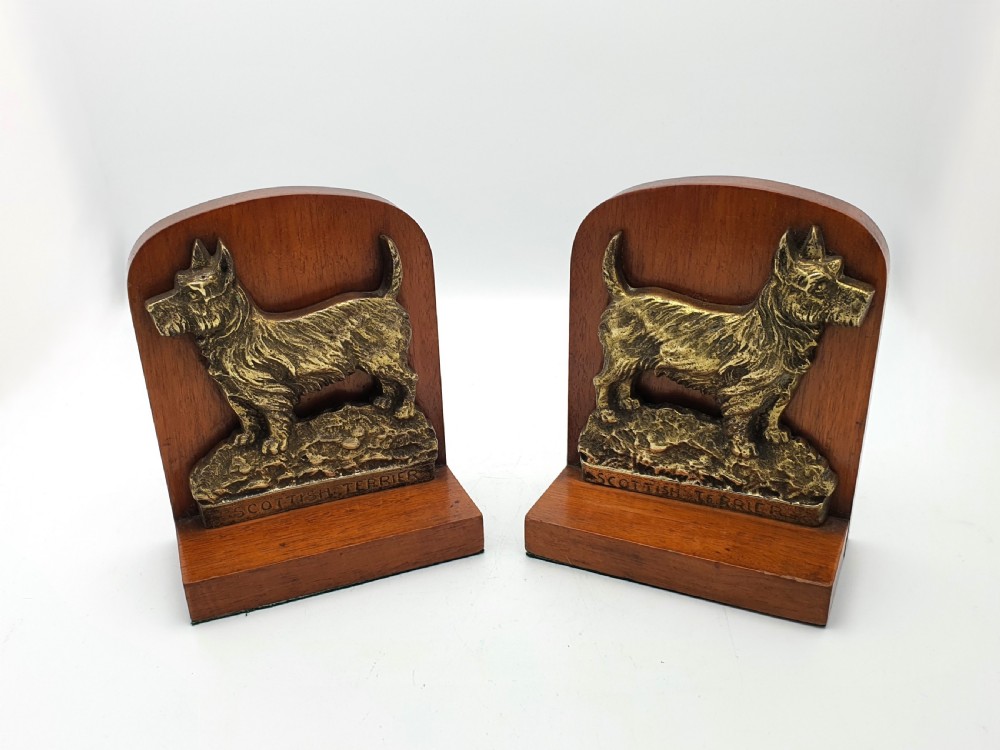 A pair of vintage 1930s wooden bookends featuring detailed cast brass reliefs of Scottish Terriers mounted on the front.