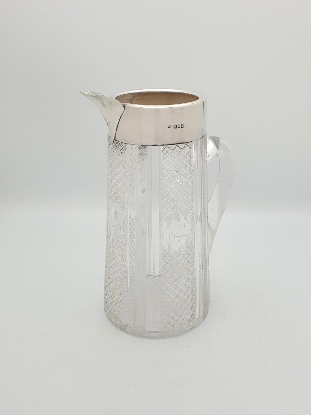 A late Victorian cut glass water jug featuring a tapered geometric cut body, an integrated glass handle, and a hallmarked sterling silver collar and spout.