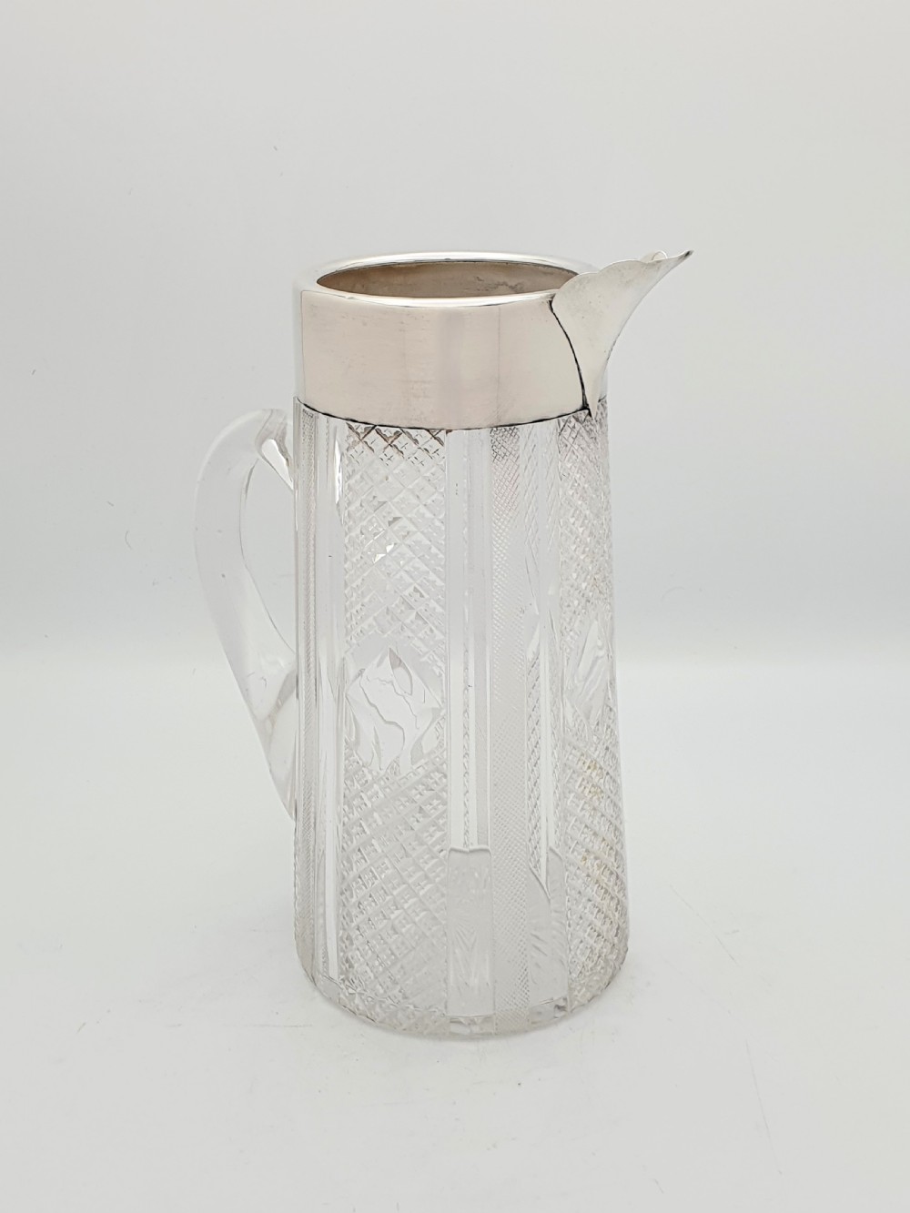 A late Victorian cut glass water jug featuring a tapered geometric cut body, an integrated glass handle, and a hallmarked sterling silver collar and spout. View II