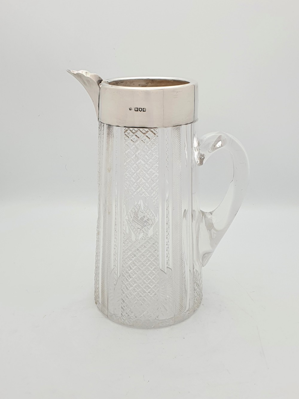 A late Victorian cut glass water jug featuring a tapered geometric cut body, an integrated glass handle, and a hallmarked sterling silver collar and spout. View III