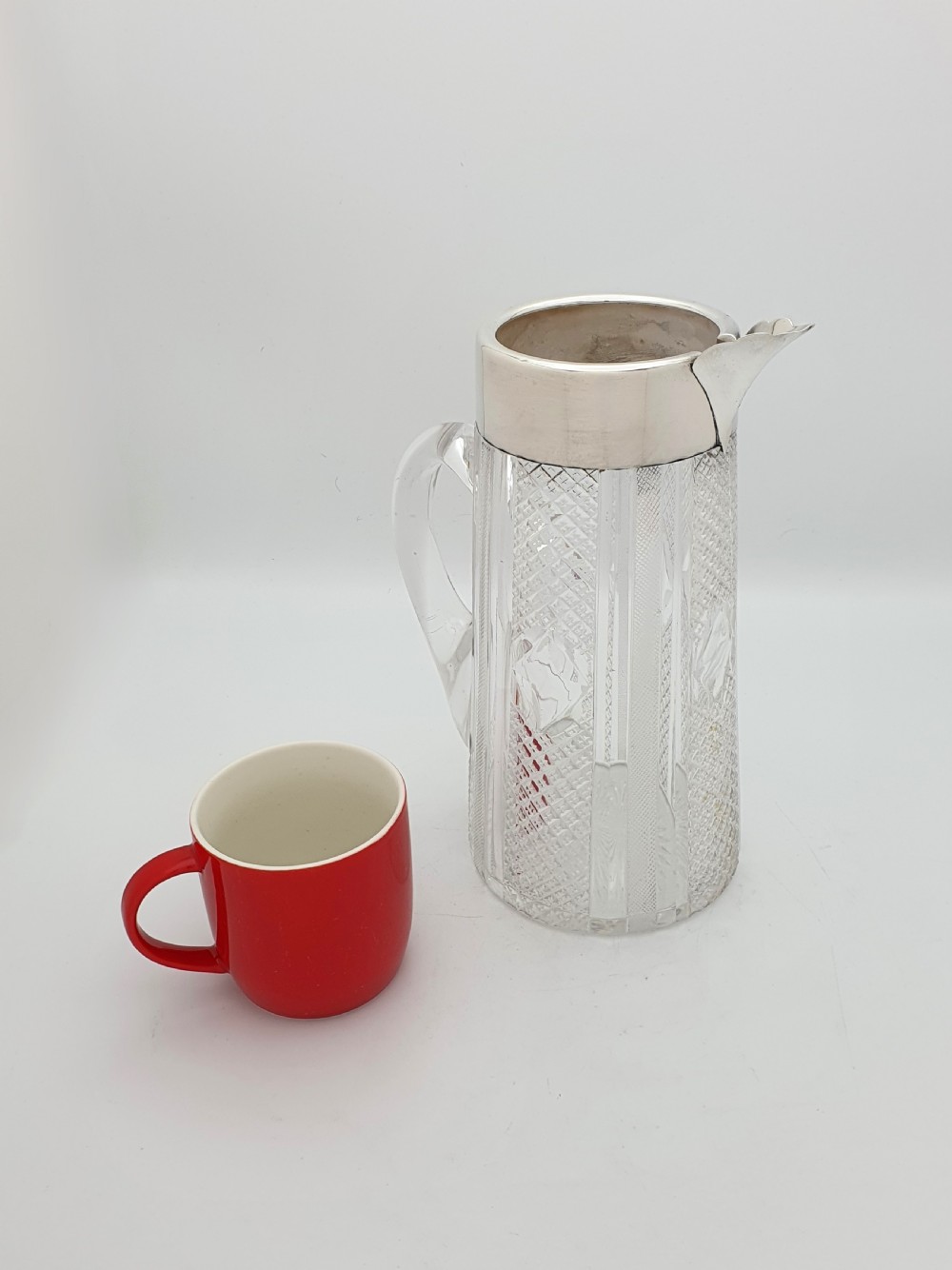 A late Victorian cut glass water jug featuring a tapered geometric cut body, an integrated glass handle, and a hallmarked sterling silver collar and spout. View V