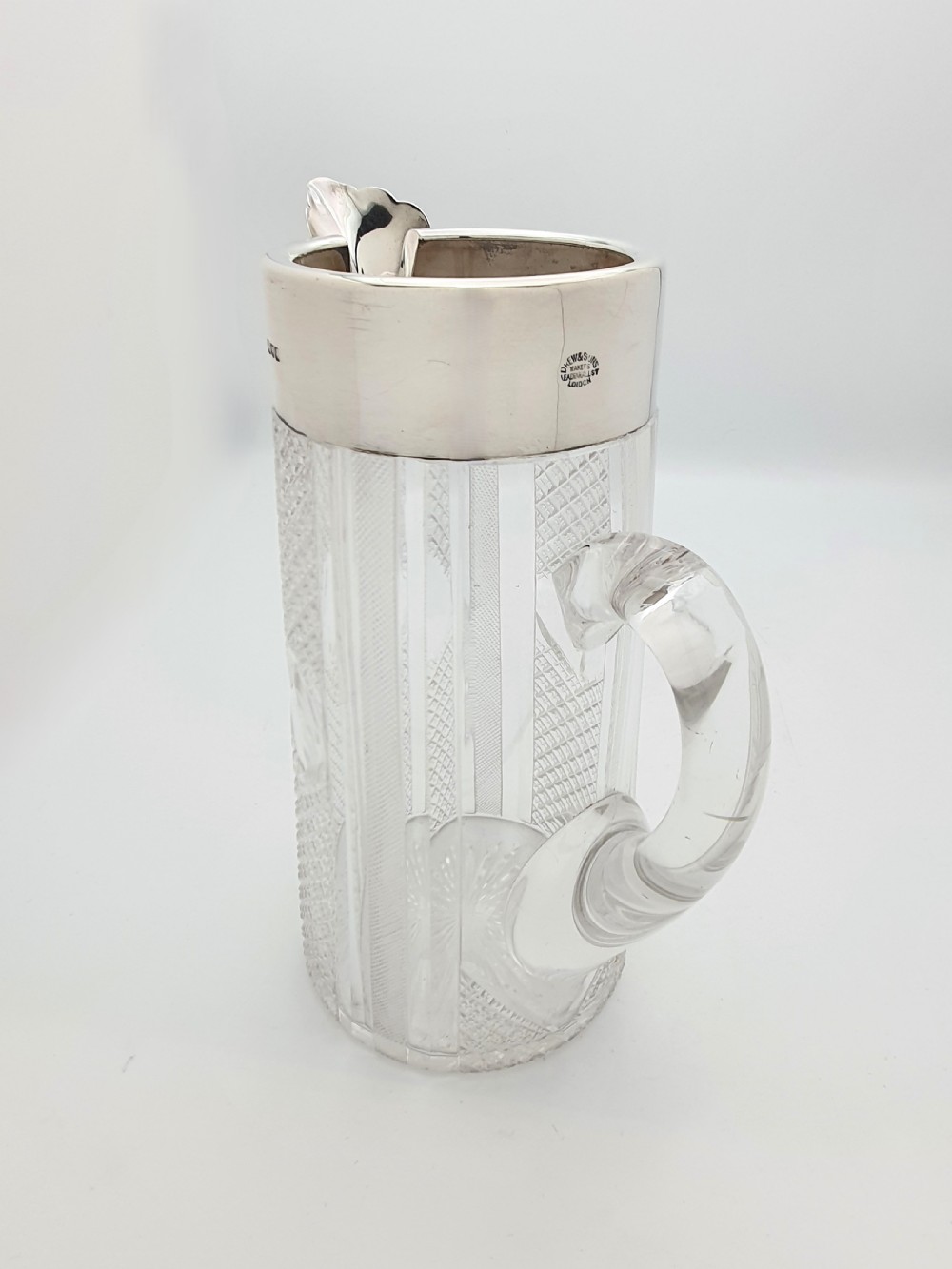 A late Victorian cut glass water jug featuring a tapered geometric cut body, an integrated glass handle, and a hallmarked sterling silver collar and spout. View VII