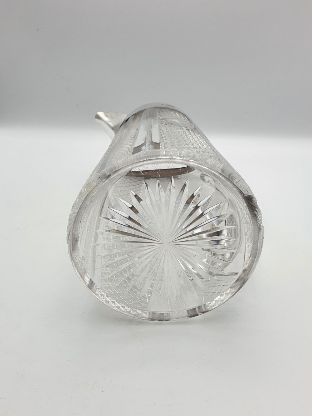 A late Victorian cut glass water jug featuring a tapered geometric cut body, an integrated glass handle, and a hallmarked sterling silver collar and spout. View VIII