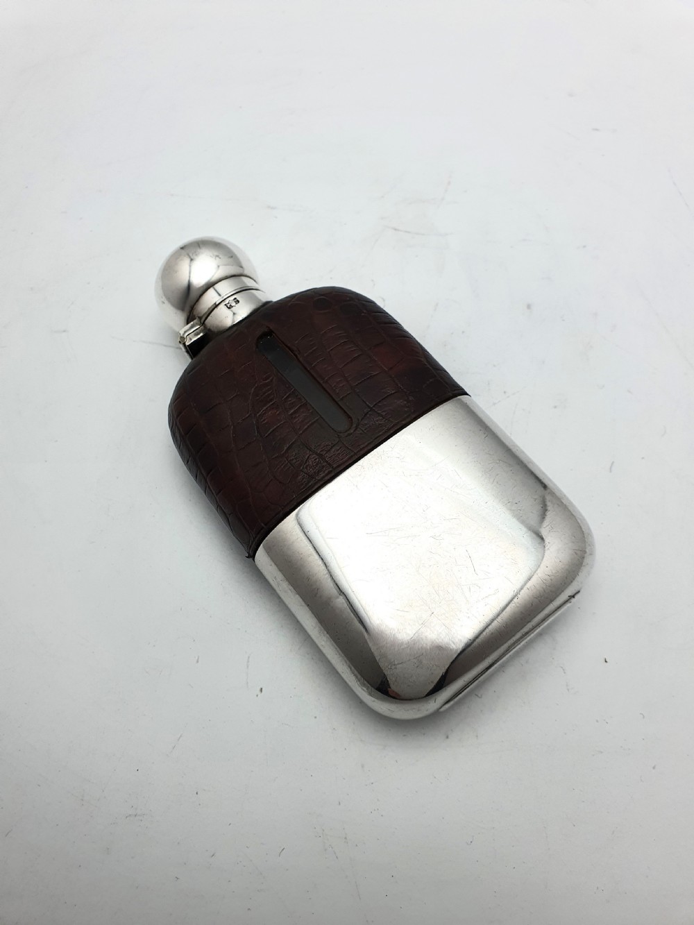 An antique 1920s silver-plated hip flask featuring a dark brown crocodile-embossed leather upper sleeve with a sight window and a silver-plated bayonet cap.