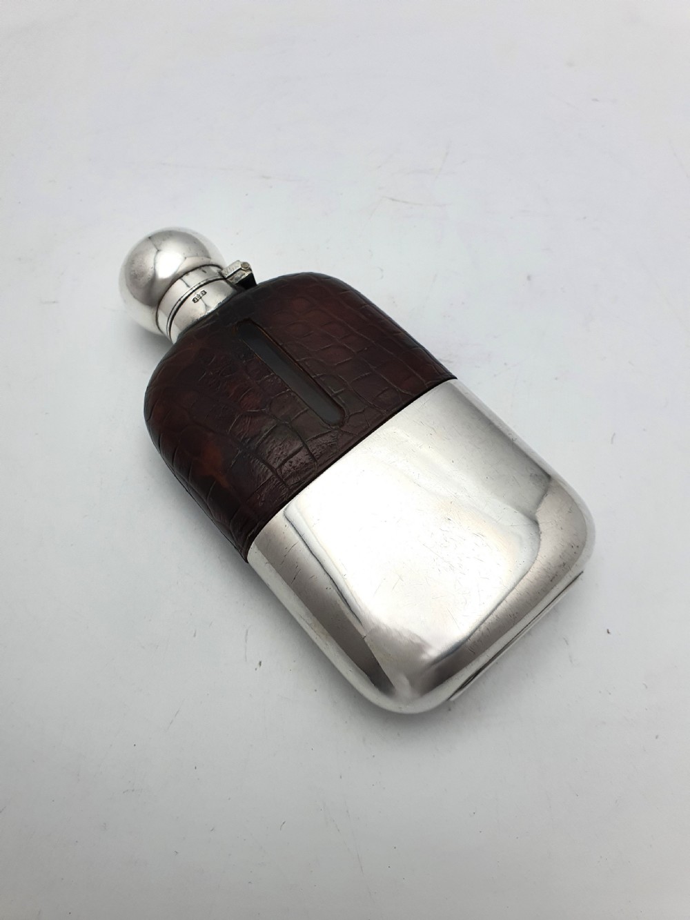 An antique 1920s silver-plated hip flask featuring a dark brown crocodile-embossed leather upper sleeve with a sight window and a silver-plated bayonet cap. View II