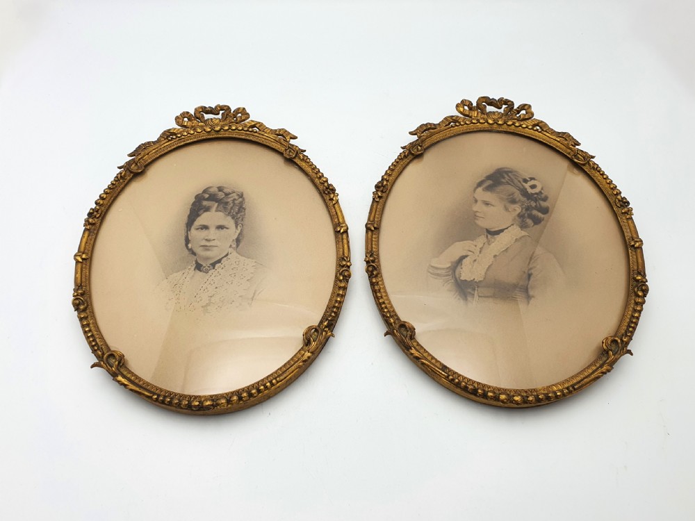 A pair of oval gilt brass photo frames featuring decorative ribbon bow crests and beaded borders containing sepia portrait photographs. View III