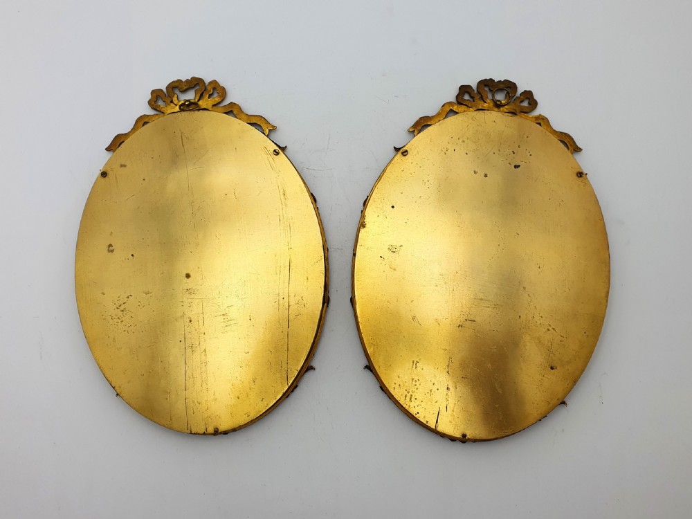 A pair of oval gilt brass photo frames featuring decorative ribbon bow crests and beaded borders containing sepia portrait photographs. View IV