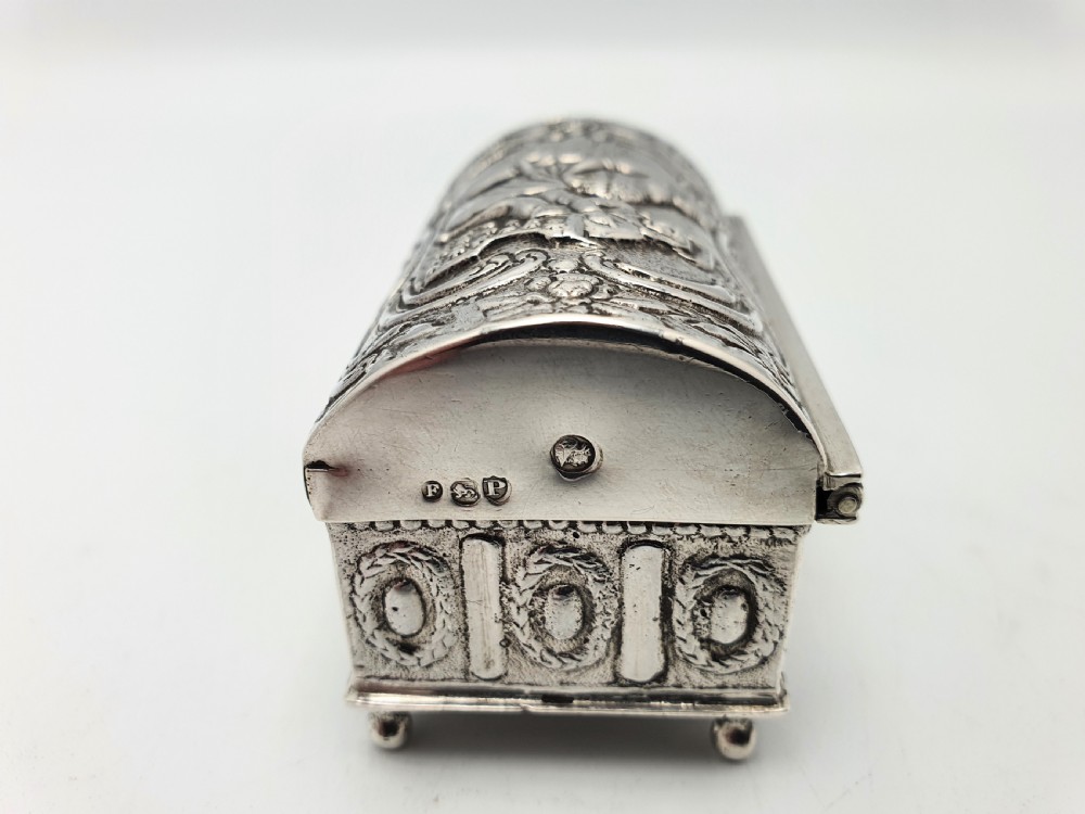 An embossed silver rectangular trinket box featuring a domed lid decorated with figures in relief and supported by four small ball feet. View IX