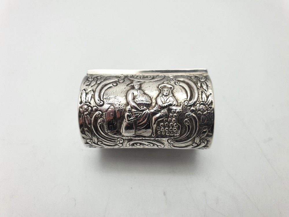 An embossed silver rectangular trinket box featuring a domed lid decorated with figures in relief and supported by four small ball feet. View X