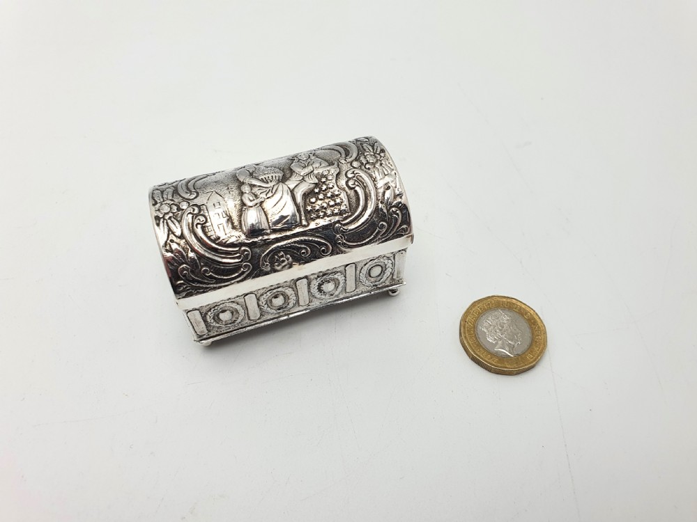 An embossed silver rectangular trinket box featuring a domed lid decorated with figures in relief and supported by four small ball feet. View XI
