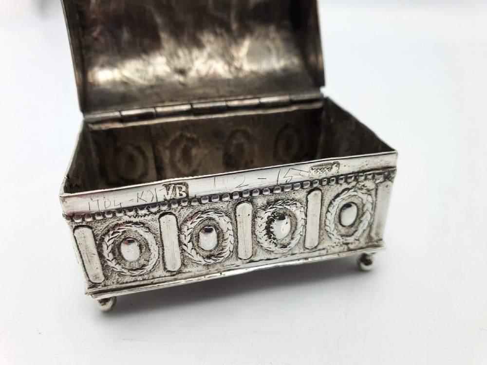 An embossed silver rectangular trinket box featuring a domed lid decorated with figures in relief and supported by four small ball feet. View XVI