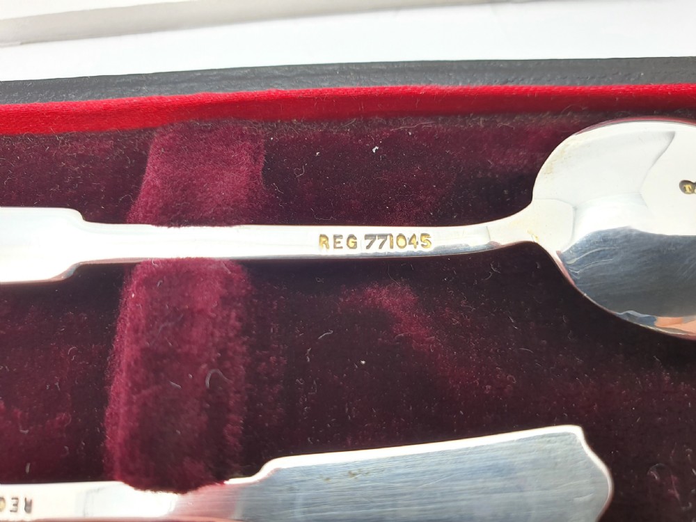 A set of six sterling silver teaspoons featuring green and blue geometric enamelled handles presented inside a fitted black velvet case with a red silk lid lining. View V