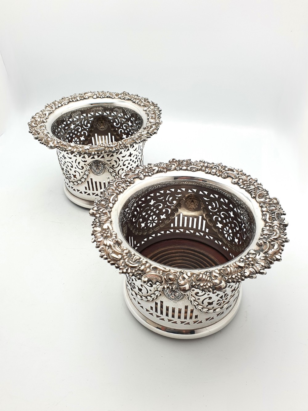A pair of circular silver-plated wine coasters with pierced fretwork sides, garland swags, medallion motifs, and decorative rims. View II
