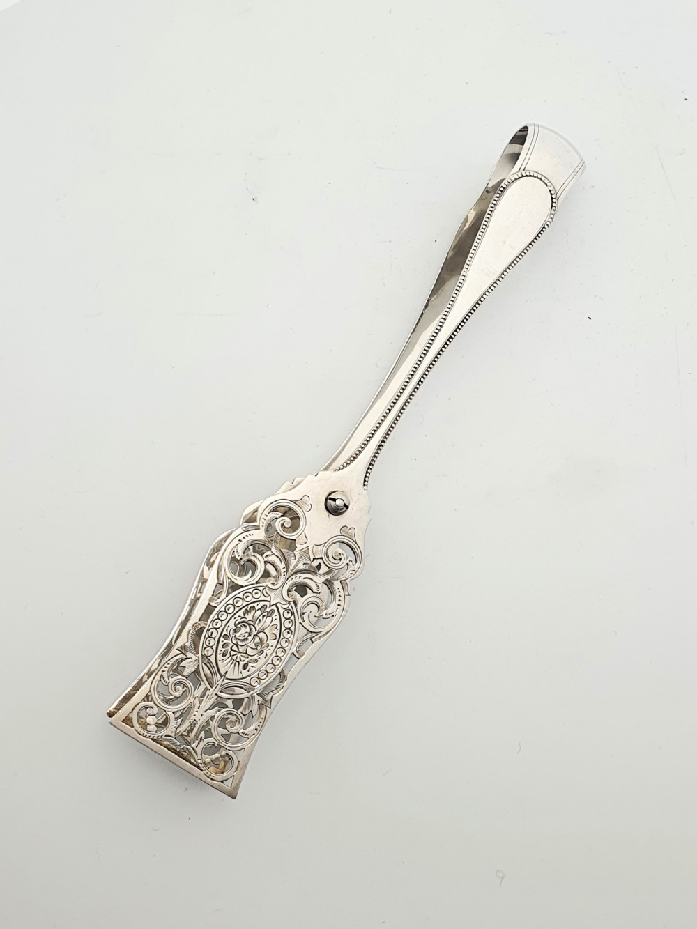 Late Victorian sterling silver serving tongs with intricately pierced scrollwork blades and beaded edge details.