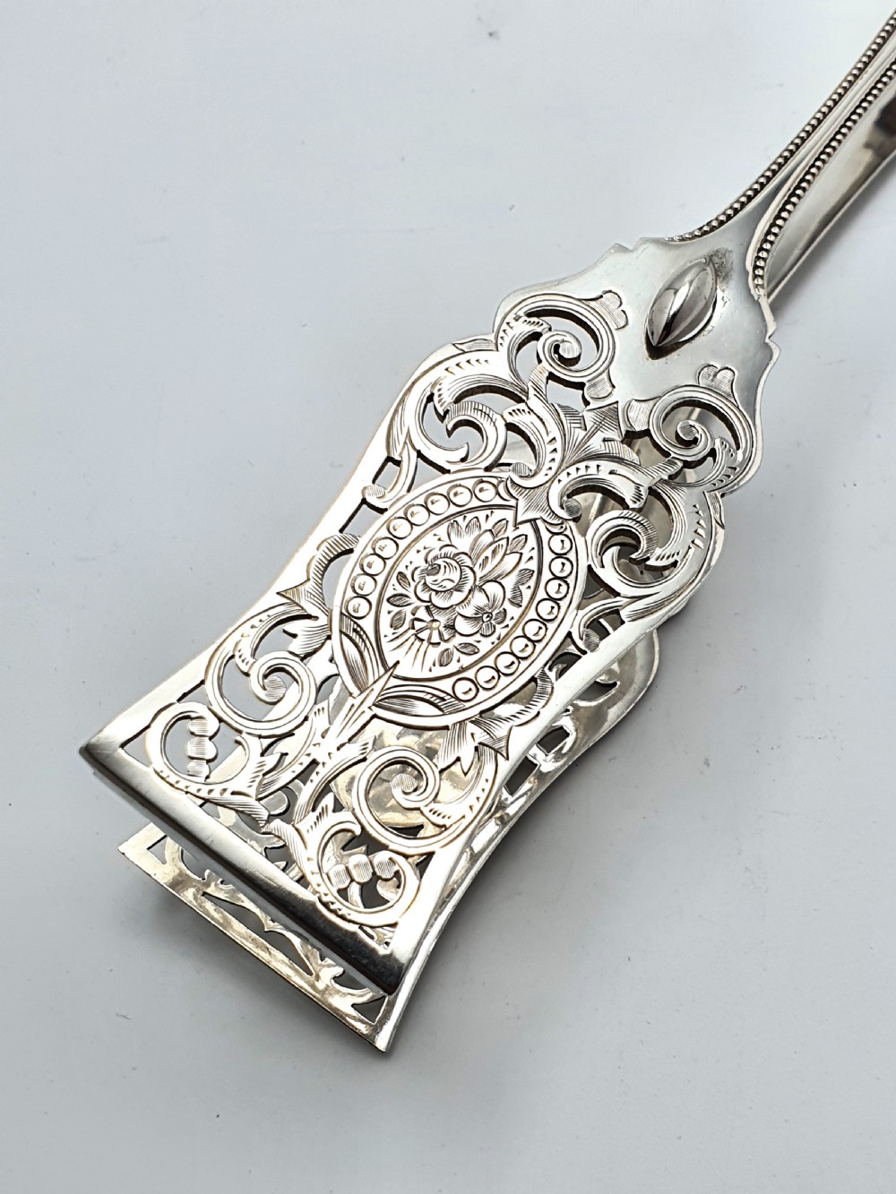 Late Victorian sterling silver serving tongs with intricately pierced scrollwork blades and beaded edge details. View II